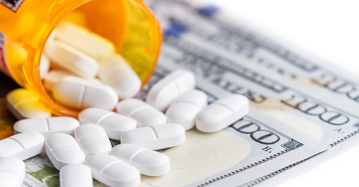 close up of a prescription bottle with white pills falling out on top of a group of hundred dollar bills