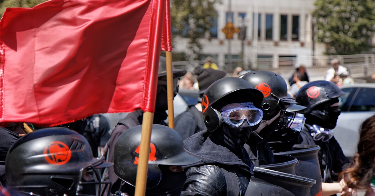 Members of Antifa dressed in black with covered faces and goggles march through Portland streets carrying red Antifa flag looking for those attending the Patriot Prayer rally in Portland, Oregon, in August 2018.