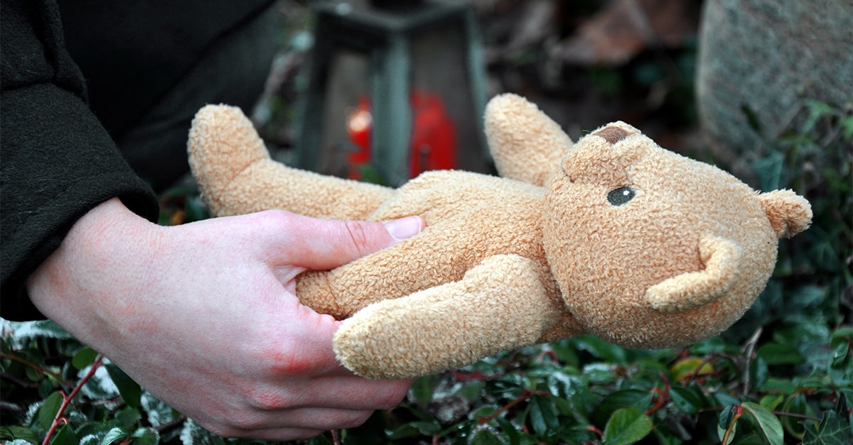 A mother lays a teddy bear on the casket of her baby during a funeral.