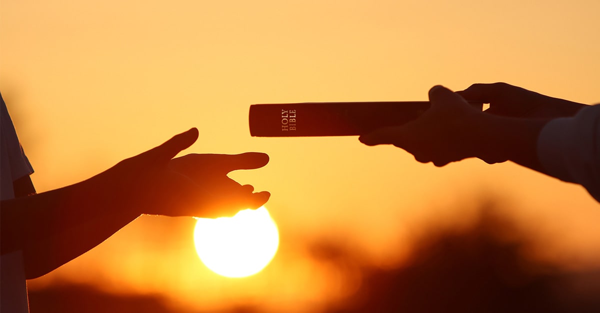 A person hands a Holy Bible to another person who is reaching for it.