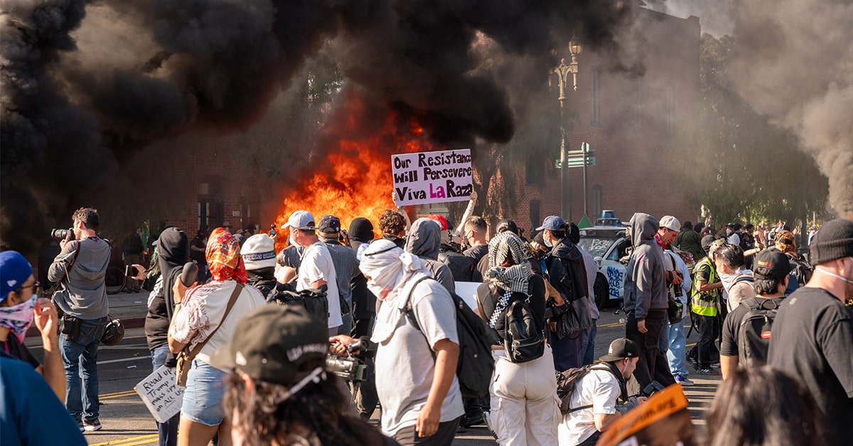 Billowing black smoke and flames rise against the sky and a mob of anti-ICE protesters chant in the street after they set self-driving taxis on fire in Los Angeles, California, on April 8, 2025.