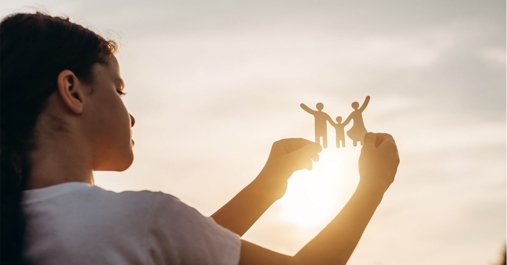 A girl holds up a paper cutout depicting a family.