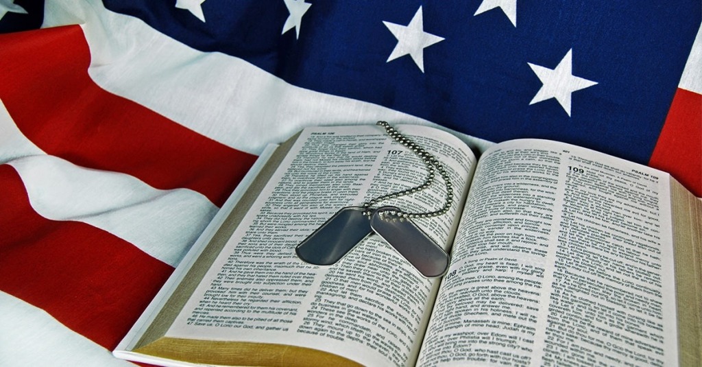 A photo of military dog tags layign on a Bible that lays on an American flag.
